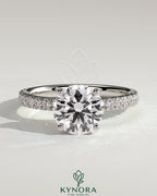 Kynora CJ 2ct round claw solitaire engagement ring with hidden halo and pavé band, featuring sparkling diamond details.