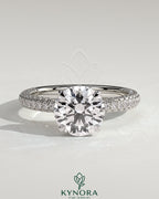 Kynora CJ 2ct round claw solitaire engagement ring with hidden halo and triple pave band, showcasing sparkling diamond details.