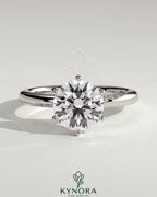Kynora CJ 2ct round claw solitaire engagement ring with sweeping micropavé band, showcasing elegant diamond setting and craftsmanship.