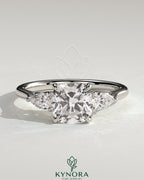 Kynora CJ 2ct cushion claw trilogy engagement ring with pear side stones and open trellis gallery design.