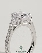 Kynora CJ 2ct elongated cushion cut trilogy engagement ring with pear side stones and pave band, elegant three-stone design.