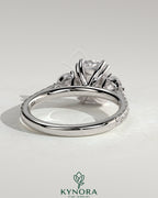 Kynora CJ 2ct elongated cushion double claw trilogy engagement ring with round side stones, pave band, and cathedral setting.