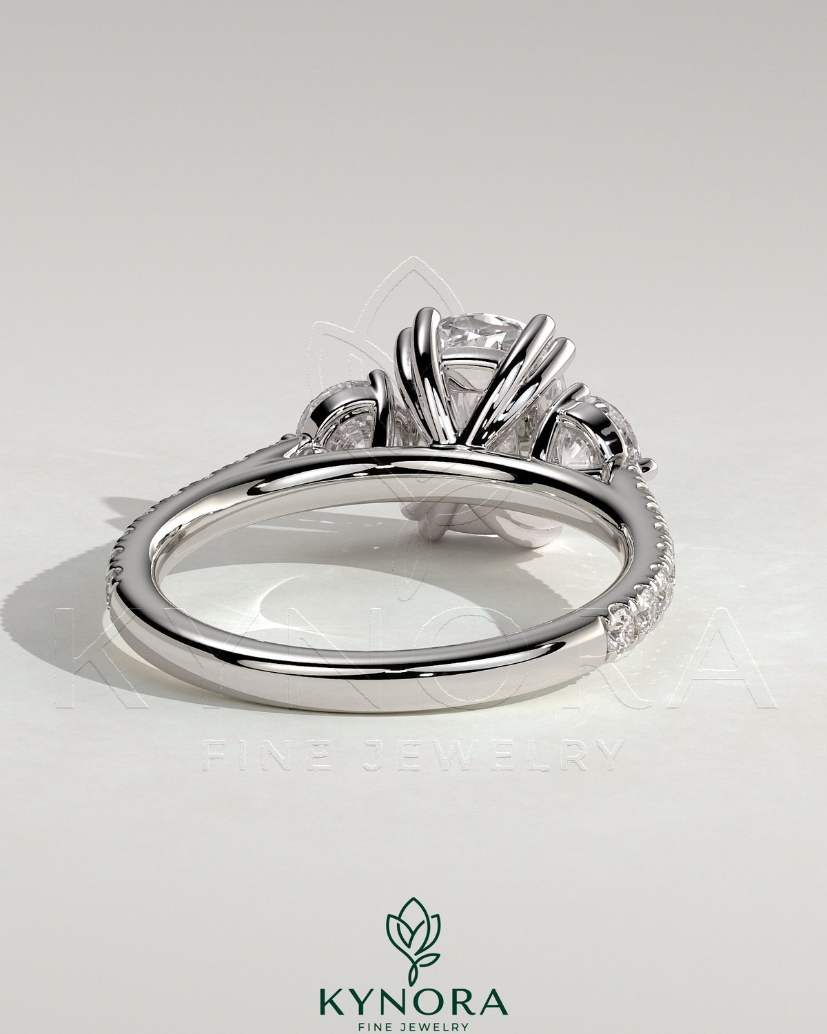 Kynora CJ 2ct elongated cushion double claw trilogy engagement ring with round side stones, pave band, and cathedral setting.
