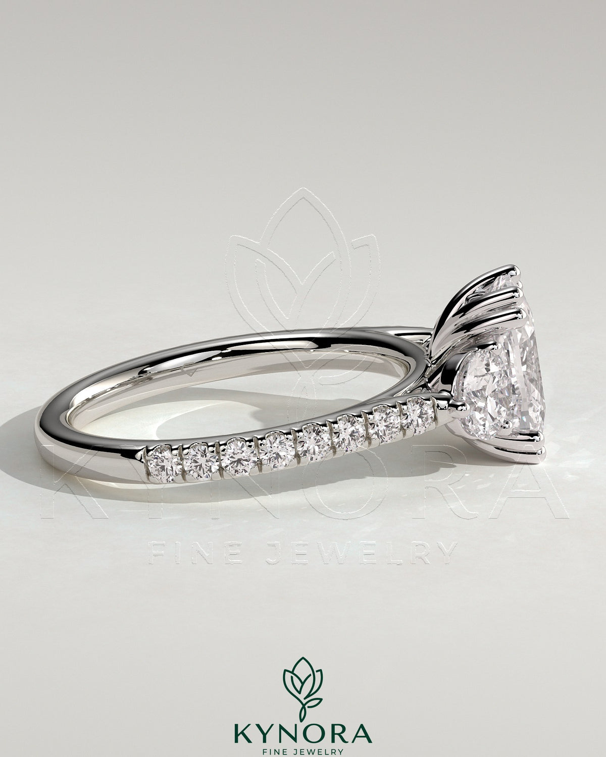 Kynora CJ 2ct elongated cushion double claw trilogy engagement ring with round side stones, pave band, and cathedral setting.