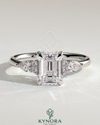 Kynora CJ 2ct emerald claw solitaire engagement ring with pear-shaped accents and round shoulder stones, three stone design.
