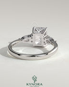 Kynora CJ 2ct emerald claw solitaire engagement ring with pear-shaped accents and round shoulder stones, elegant three stone design.