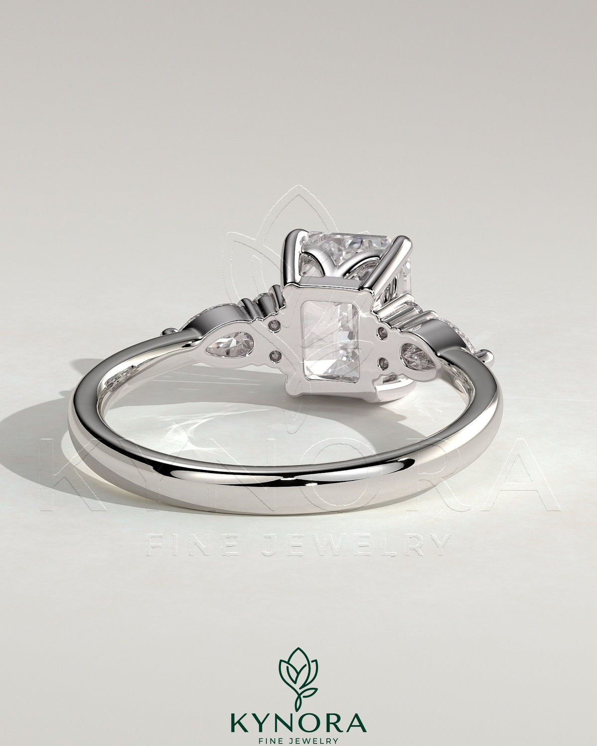 Kynora CJ 2ct emerald claw solitaire engagement ring with pear-shaped accents and round shoulder stones, elegant three stone design.