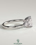 Kynora CJ 2ct emerald claw solitaire engagement ring with pear-shaped accents and round shoulder stones.