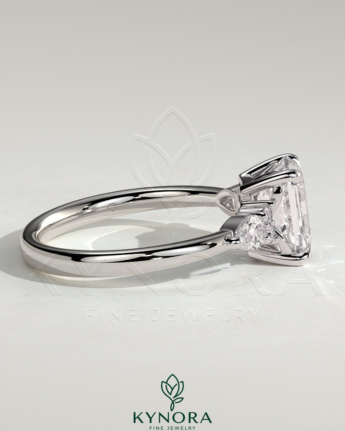 Kynora CJ 2ct emerald claw solitaire engagement ring with pear-shaped accents and round shoulder stones.