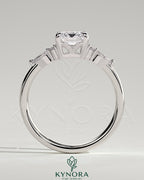 Kynora CJ 2ct emerald claw solitaire engagement ring with pear-shaped accents and round shoulder stones, three-stone design.
