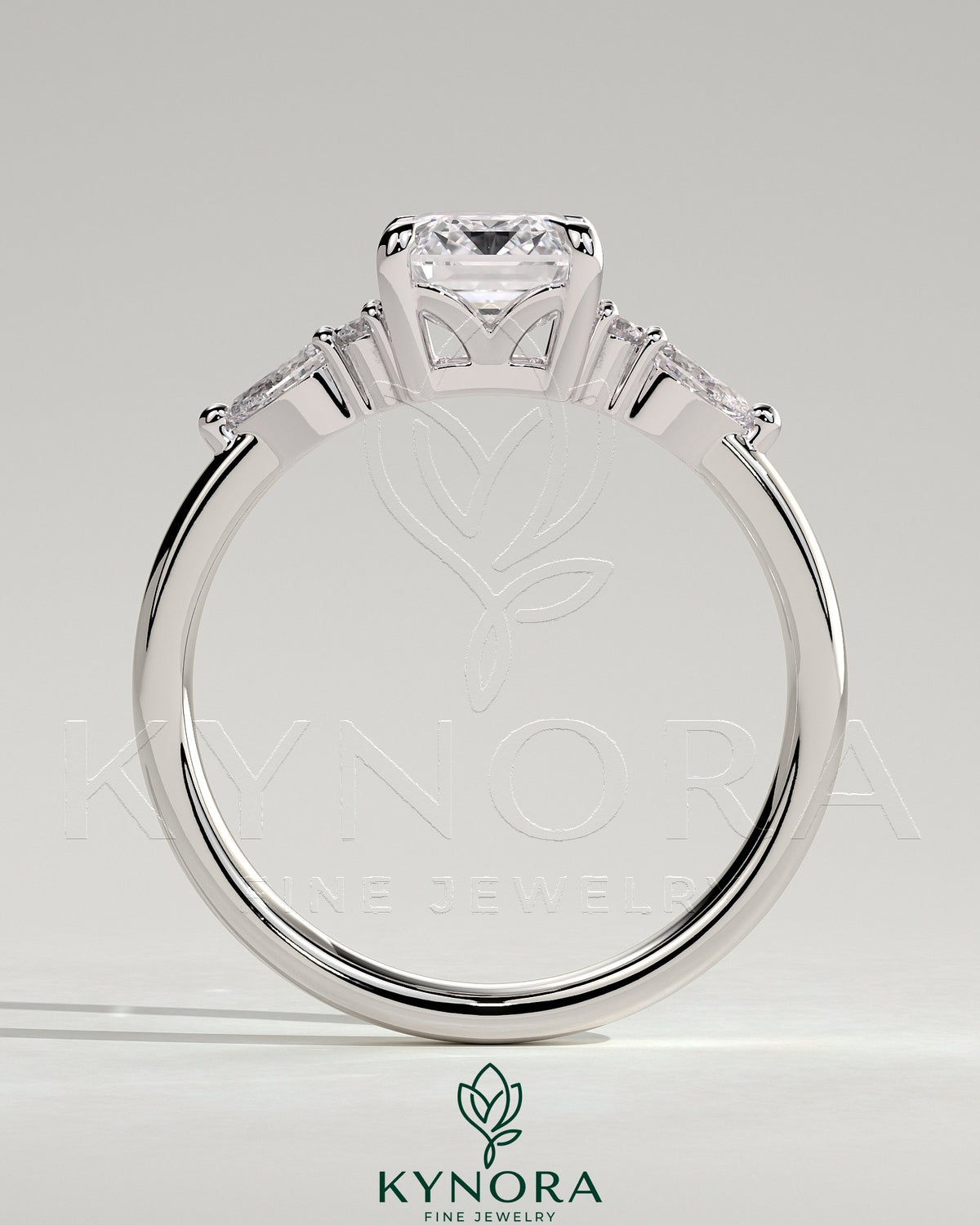 Kynora CJ 2ct emerald claw solitaire engagement ring with pear-shaped accents and round shoulder stones, three-stone design.