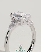 Kynora CJ 2ct emerald claw solitaire engagement ring with pear-shaped accents and round shoulder stones, three-stone design.