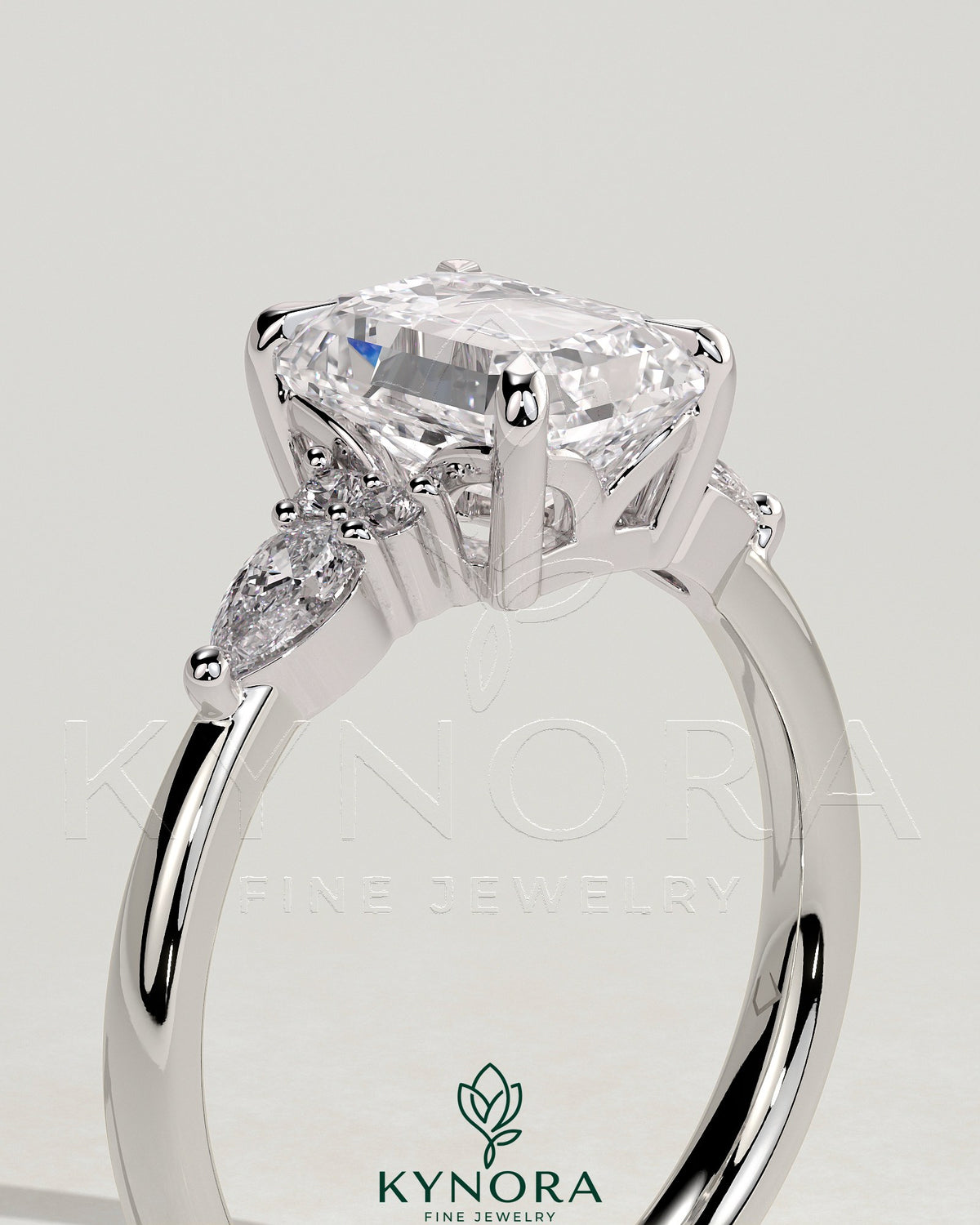 Kynora CJ 2ct emerald claw solitaire engagement ring with pear-shaped accents and round shoulder stones, three-stone design.