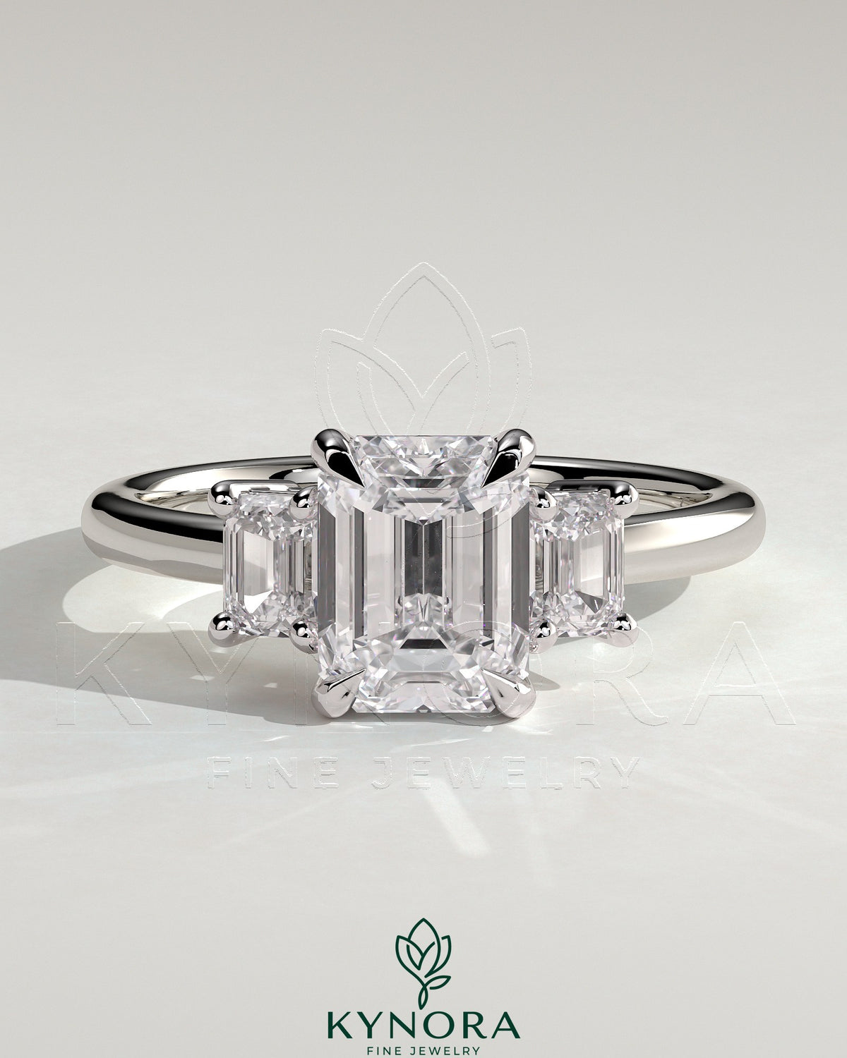 Kynora CJ 2ct Emerald Claw Trilogy engagement ring with emerald side stones and low setting, showcasing a three-stone design. Main image