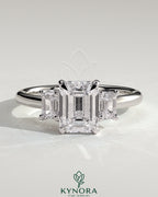 Kynora CJ 2ct Emerald Claw Trilogy engagement ring with emerald side stones and low setting, showcasing a three-stone design.