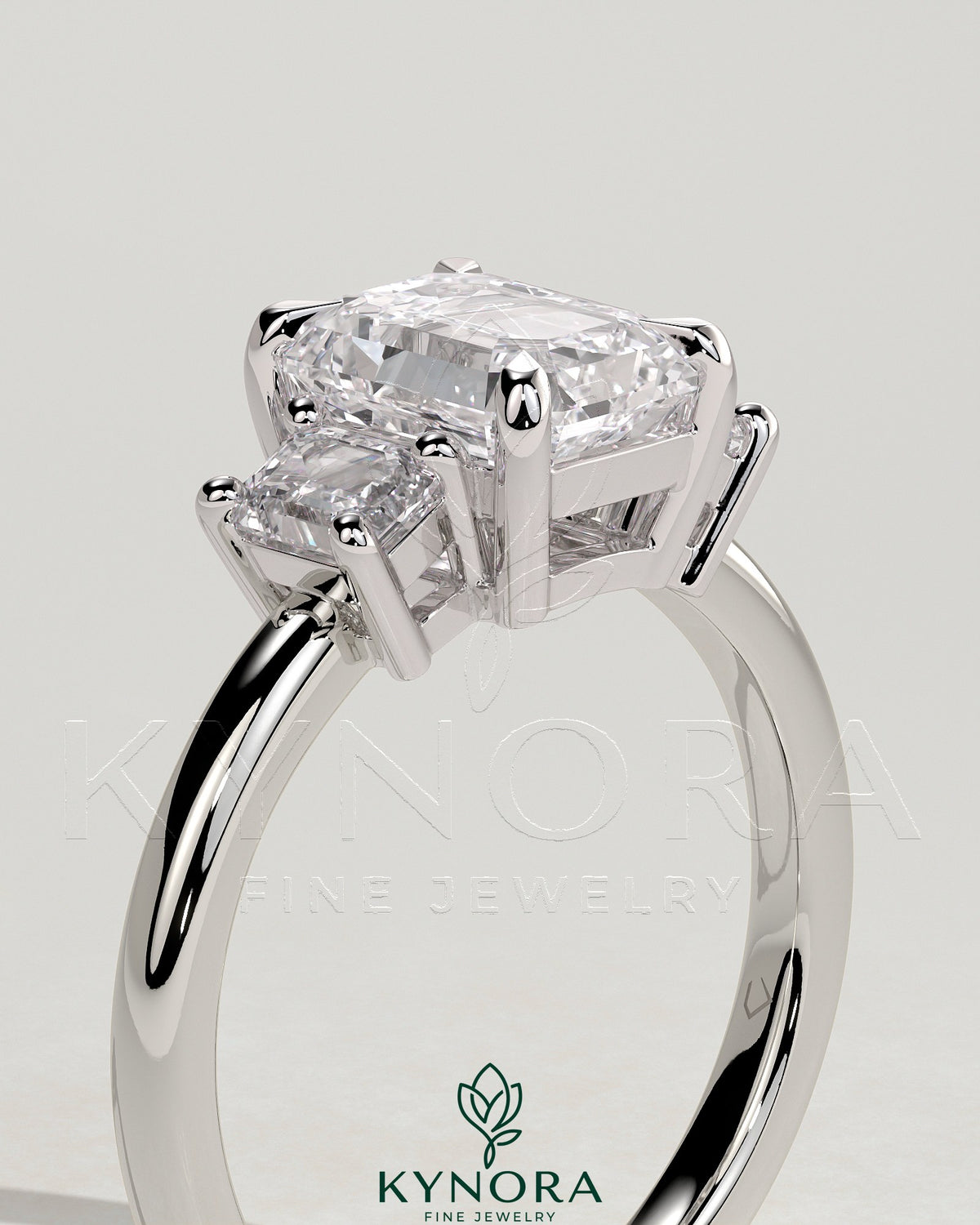 Kynora CJ 2ct emerald claw trilogy engagement ring with emerald side stones and low setting, showcasing a three-stone design.