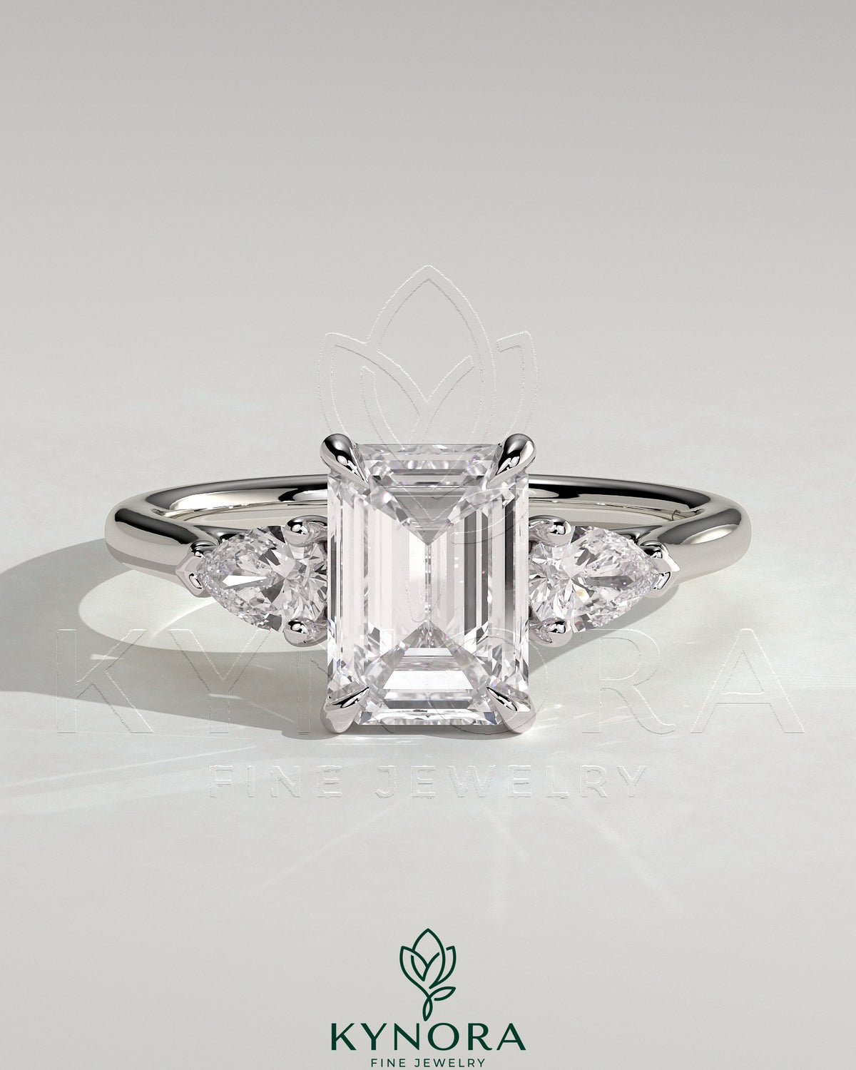 Kynora CJ 2ct emerald claw trilogy engagement ring with pear side stones and cathedral setting in yellow gold.