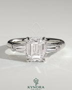 Kynora CJ 2ct emerald claw trilogy engagement ring with tapered baguette side stones and cathedral setting, detailed close-up image.