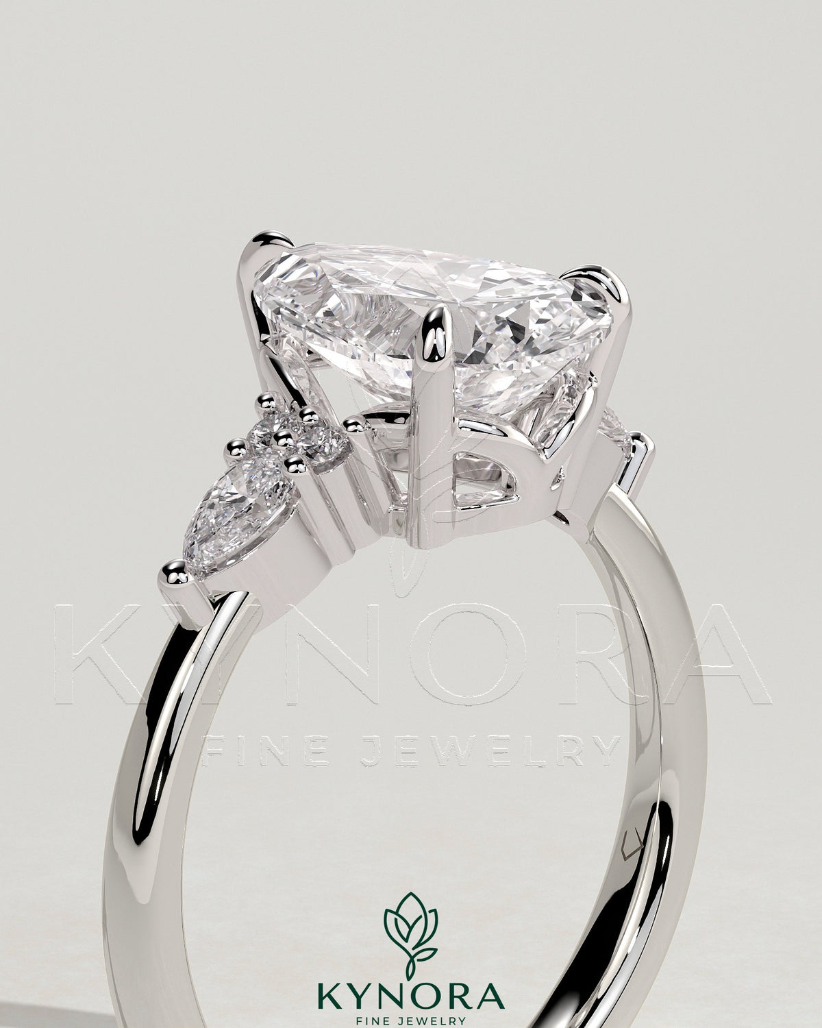 Kynora CJ 2ct pear claw solitaire engagement ring with pear accents and round shoulder stones in a three-stone design.