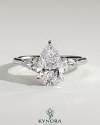Kynora CJ 2ct pear claw trilogy engagement ring with side stones and cathedral setting, showcasing sparkling diamond design.