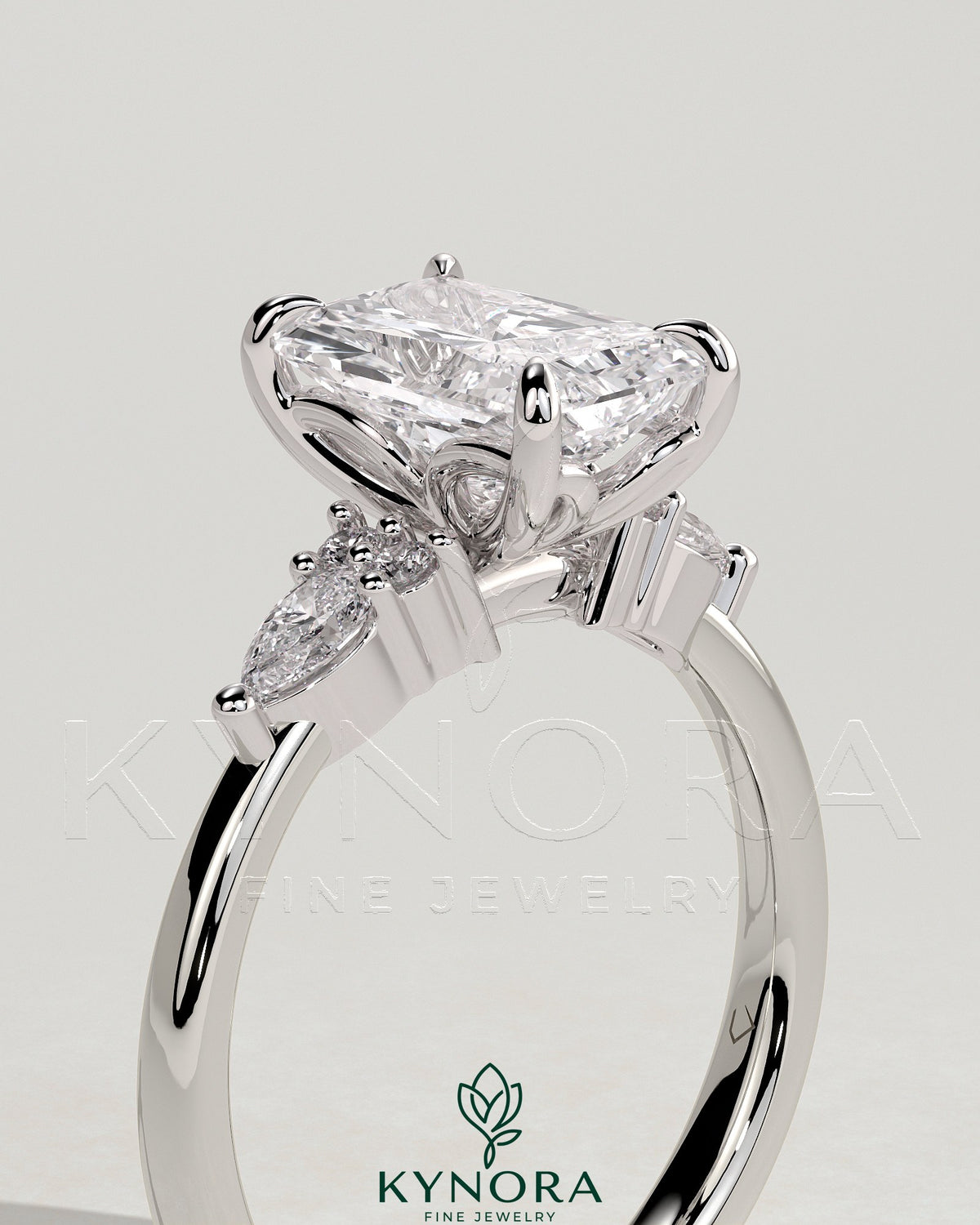 Kynora CJ three-stone engagement ring with 2ct radiant claw-set center stone, pear and round shoulder accents, elegant jewelry piece