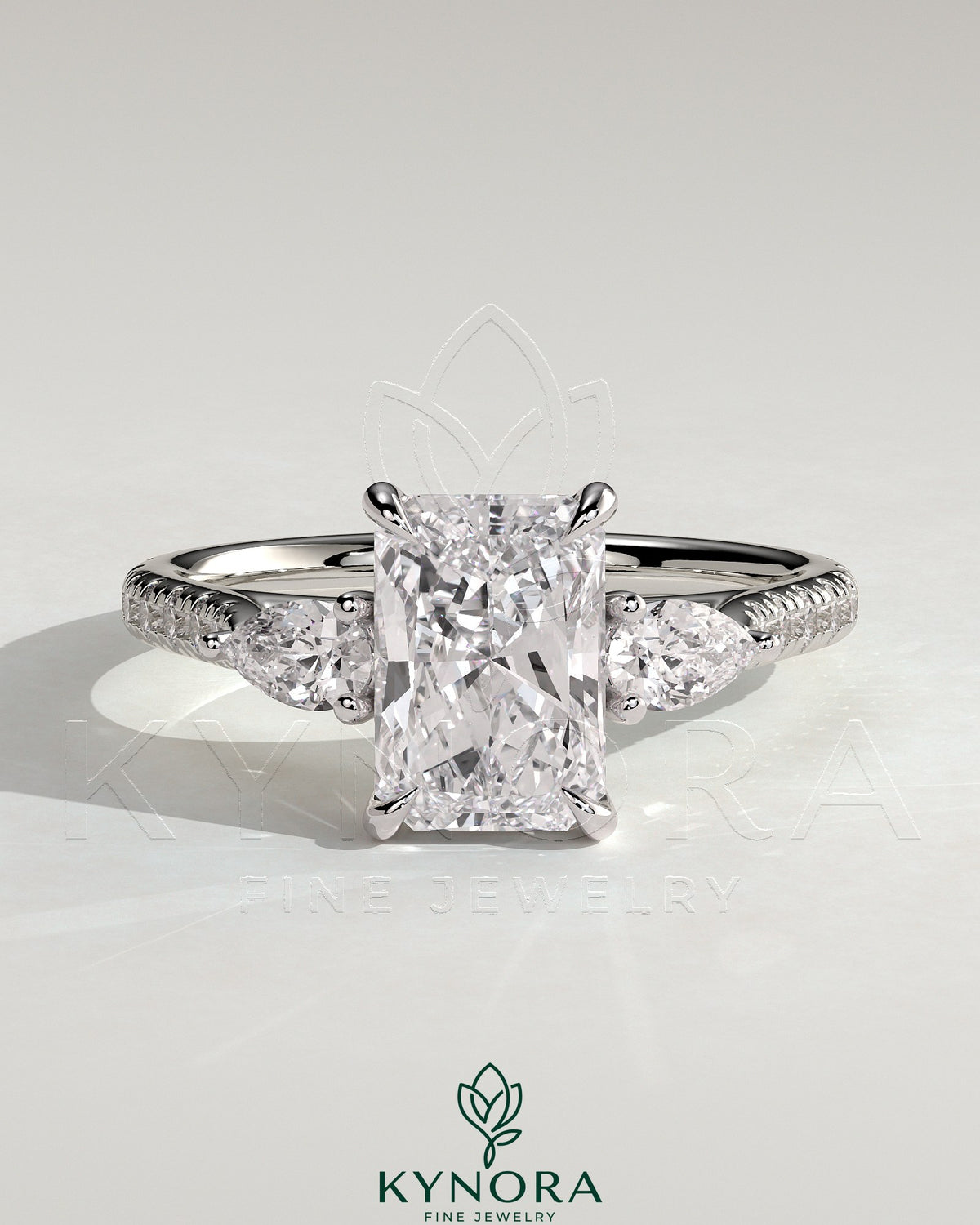 Kynora CJ 2ct radiant claw trilogy engagement ring with pear side stones and pave band, showcasing elegant diamond craftsmanship. Imagen principal del producto