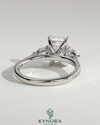 Kynora CJ 2ct radiant claw trilogy engagement ring with pear side stones and pave band, featuring a sparkling three-stone design.