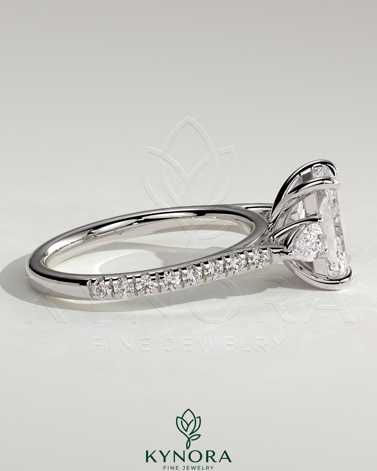 Kynora CJ 2ct radiant claw trilogy engagement ring with pear side stones and pave band, featuring a sparkling three-stone design.