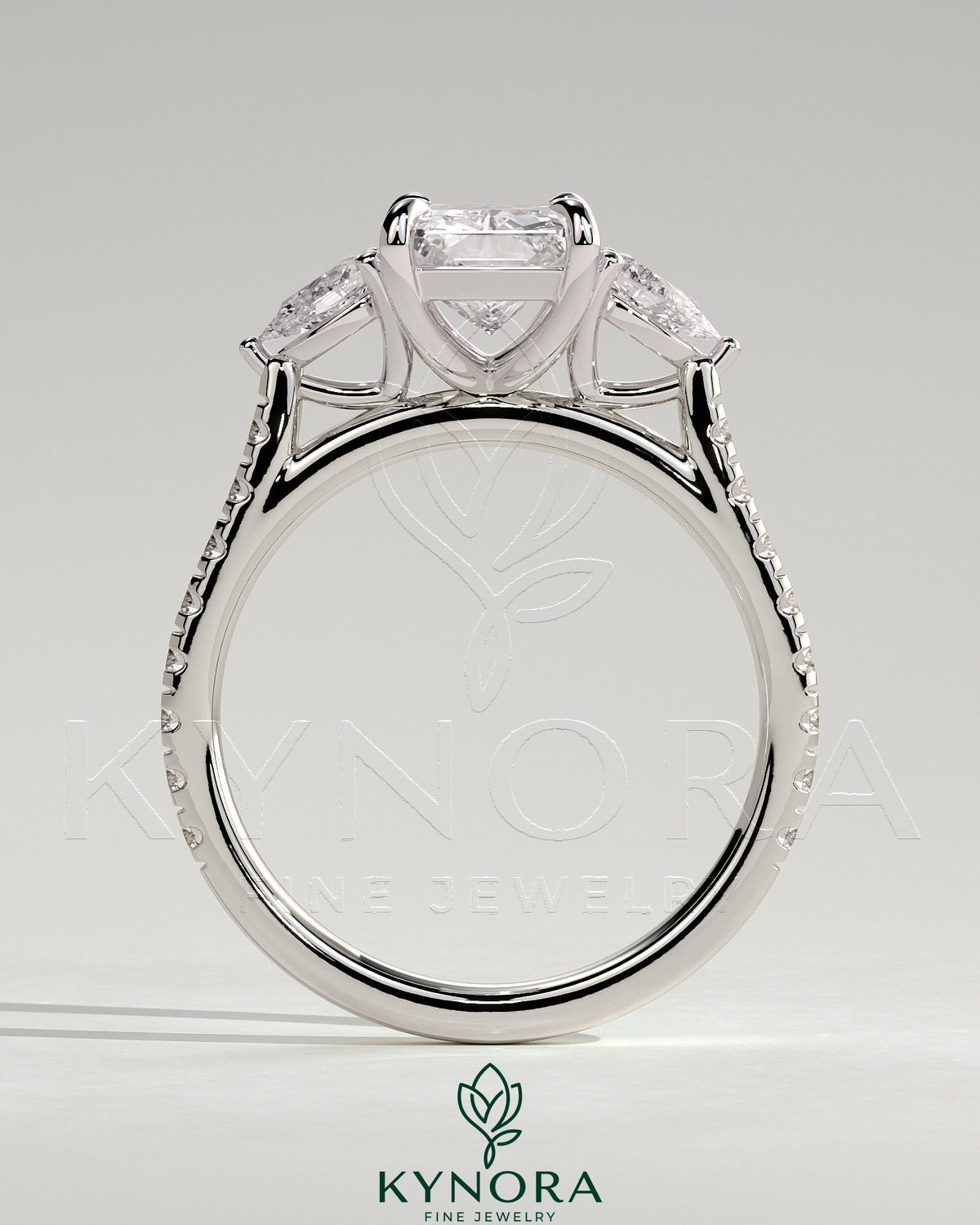 Kynora CJ 2ct radiant claw trilogy engagement ring with pear side stones and pave band featuring sparkling diamonds.
