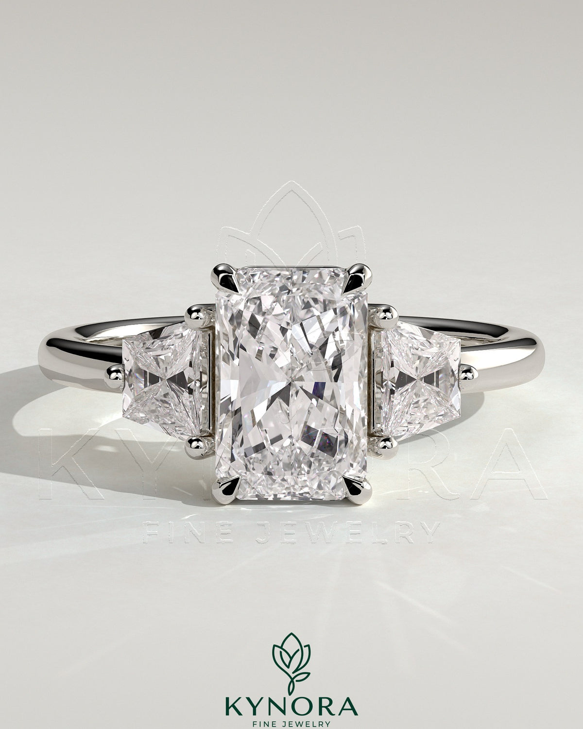 Kynora CJ 2ct radiant claw trilogy engagement ring with trapezoid side stones in a low setting, showcasing elegant diamond design. Imagen principal del producto