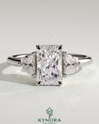 Kynora CJ 2ct radiant claw trilogy engagement ring with trapezoid side stones in a low setting, showcasing elegant diamond design.