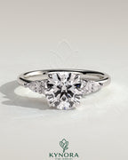 Kynora CJ 2ct round claw solitaire engagement ring with pear-shaped accents and round shoulder stones, three stone design.