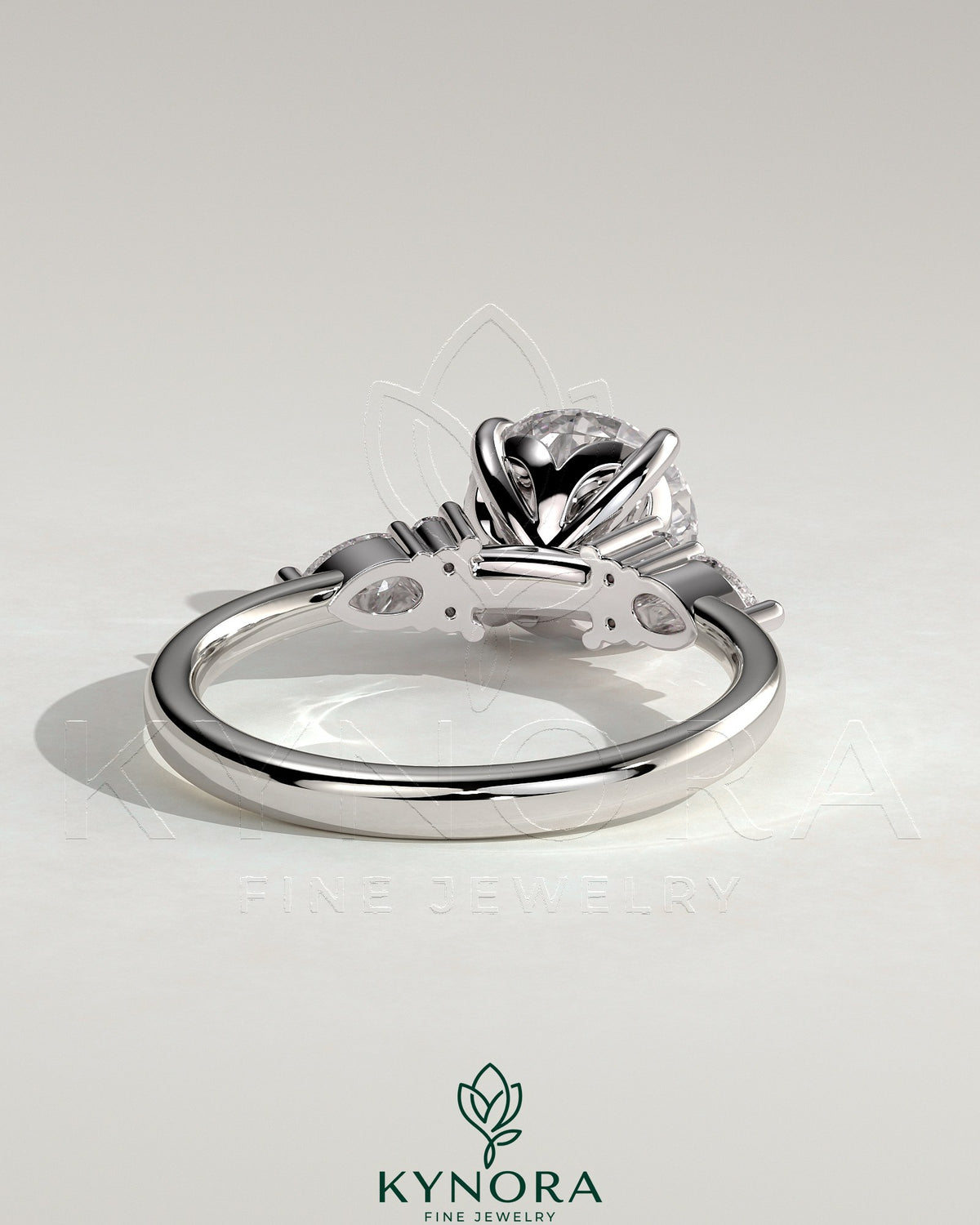 Kynora CJ three-stone engagement ring with 2-carat round claw solitaire, pear accents, and round shoulder stones in polished metal