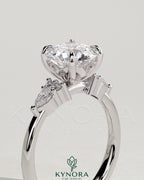 Kynora CJ 2ct round claw solitaire engagement ring with pear accents and round shoulder stones, elegant three-stone design.