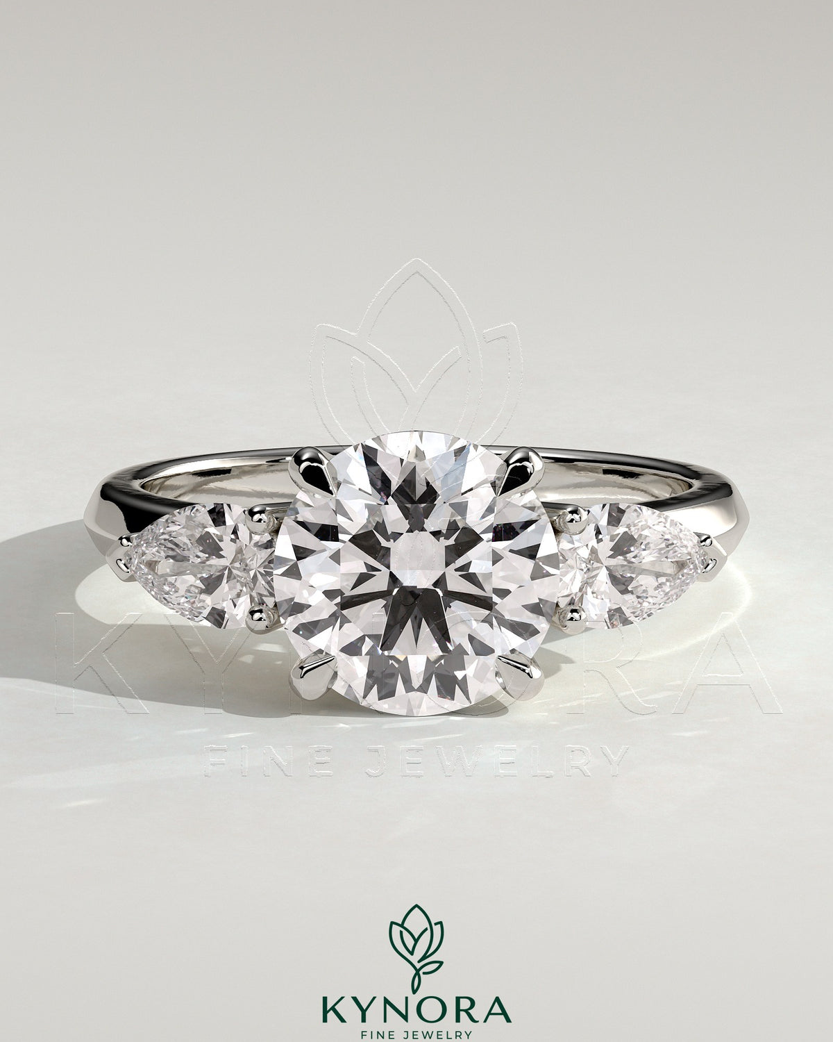 Kynora CJ three-stone engagement ring featuring a 2-carat round claw trilogy center with pear side stones and a knife edge band.