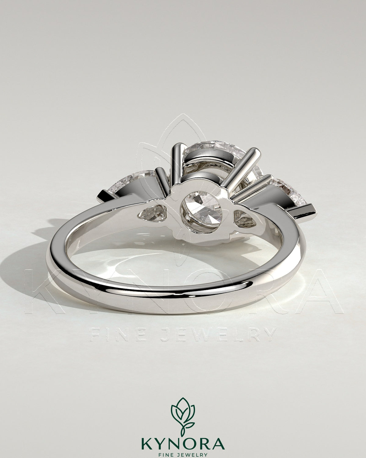 Kynora CJ 2ct round claw trilogy engagement ring with pear side stones and knife edge band, showcasing elegant diamond craftsmanship.