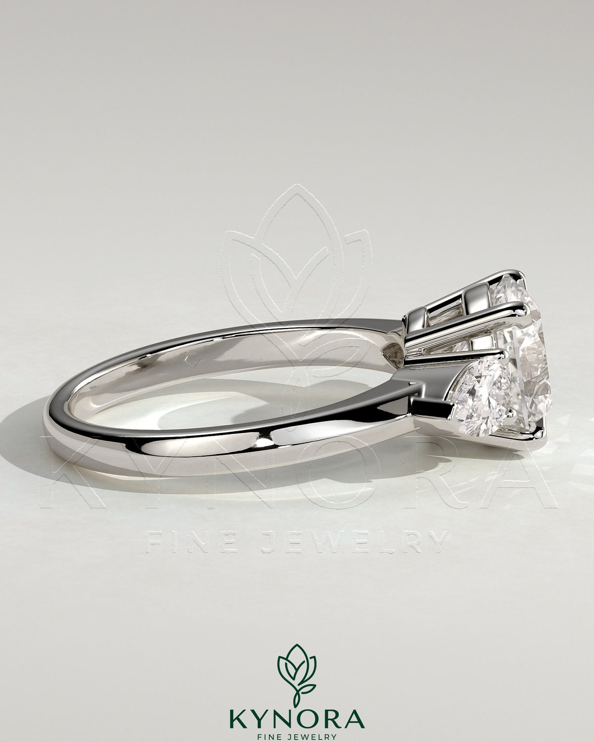 Kynora CJ 2ct round claw trilogy engagement ring with pear side stones and knife edge band, showcasing elegant craftsmanship.