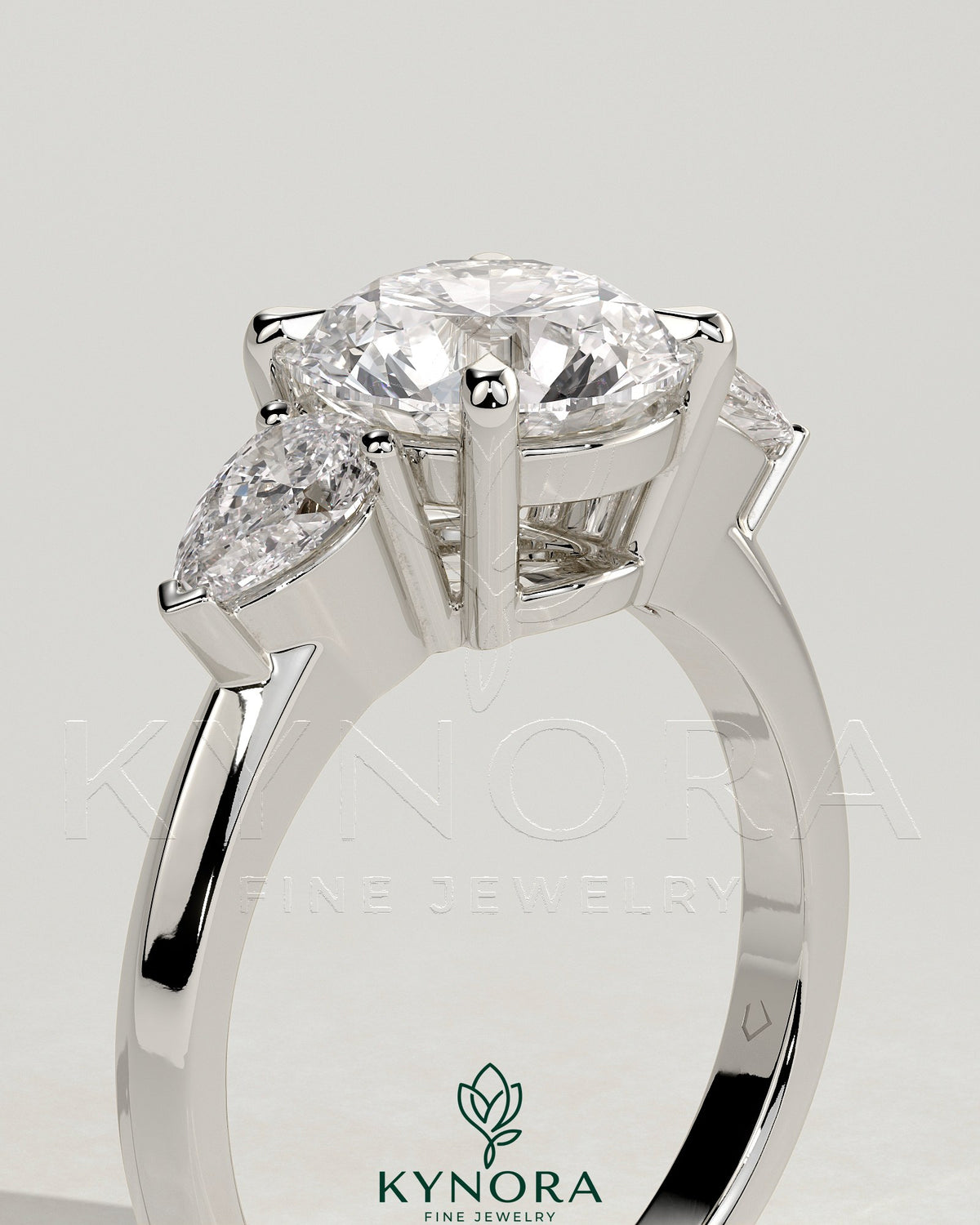 Kynora CJ 2ct round claw trilogy engagement ring with pear side stones and knife edge band, sparkling and elegant jewelry piece.