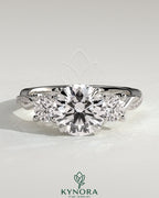 Kynora CJ three stone engagement ring with 2ct round claw trilogy, round side stones, twisted pave band, and trellis gallery design