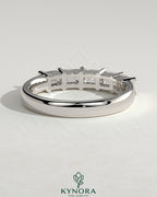 Kynora CJ emerald east-west wedding band with closed basket setting, featuring a central emerald gemstone and intricate metalwork.